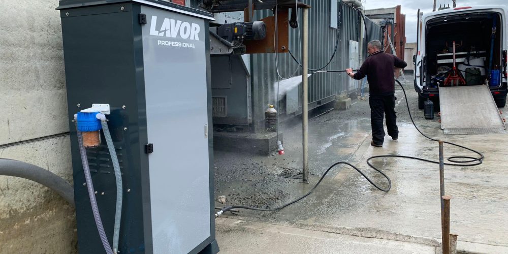 A professional ride-on industrial floor sweeper clearing winter debris, sand, and excess gritting salt from a commercial car park and pavement walkway layout.