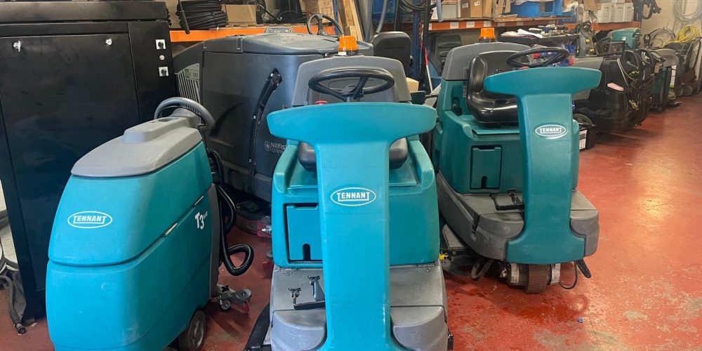 A lineup of fully restored and refurbished Tennant commercial walk-behind floor scrubber dryers, fully tested and ready for deployment in industrial environments.