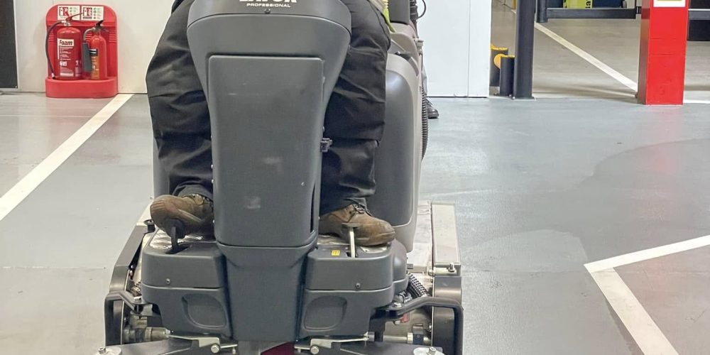 A live product demonstration of the Lavorwash Duotec ride-on floor cleaning machine, highlighting its dual sweeping and scrubbing capabilities for large commercial floors.