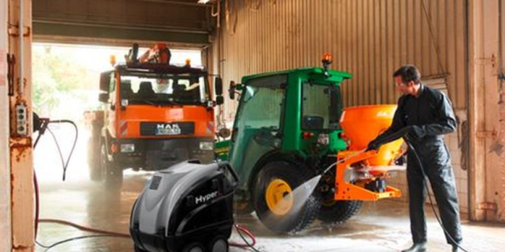 A local farmer using a professional heavy-duty hot water power washer to quickly blast thick mud and grease off a large farm tractor.