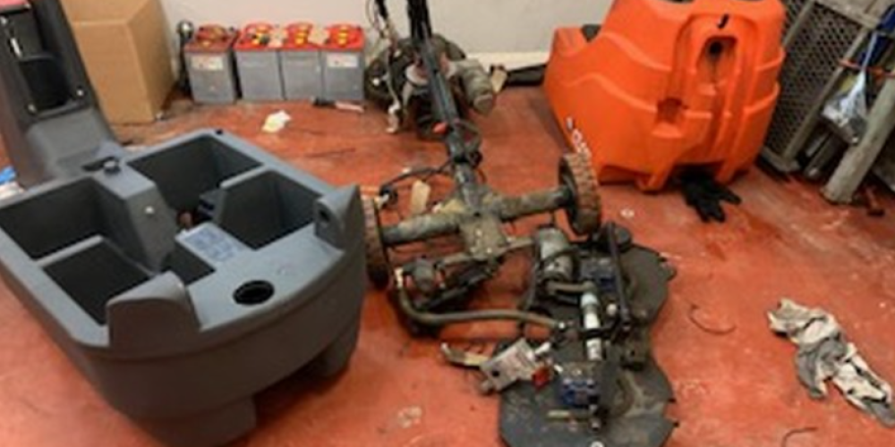 A professional service engineer repairing an industrial floor scrubber dryer machine, diagnosing mechanical faults for a local commercial client.