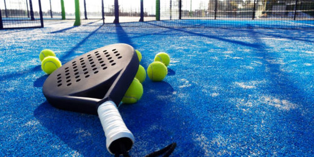 Using a pedestrian walk-behind sweeper machine on a blue artificial turf padel court to clear organic debris and maintain summer surface playability.
