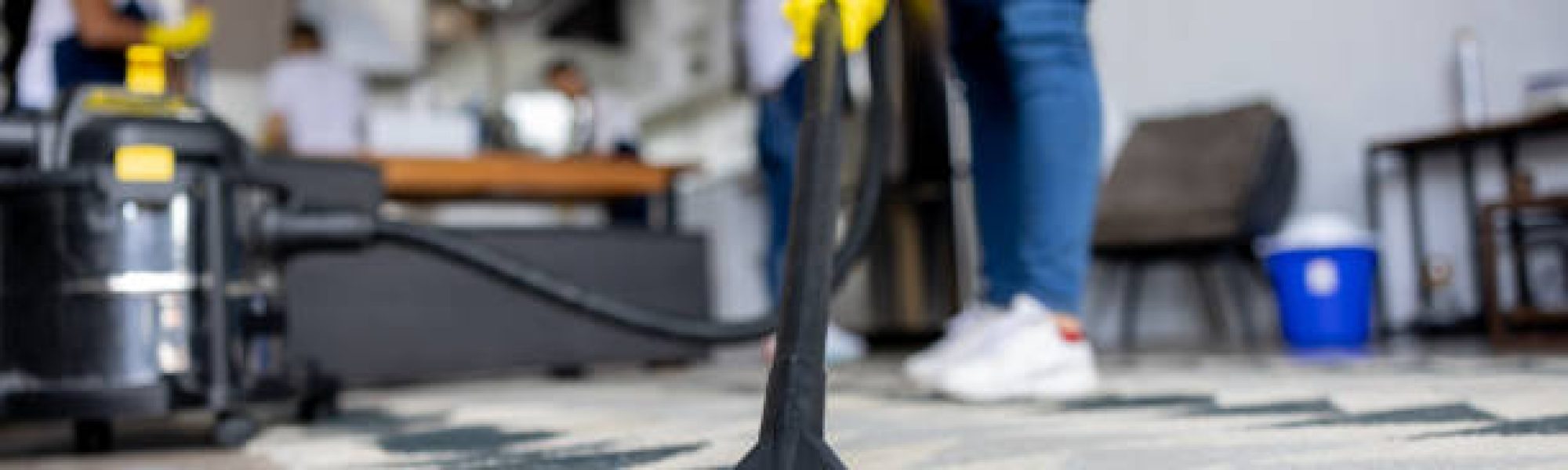Close-up on a professional cleaner vacuuming a carpet while working at an apartment - housework concepts